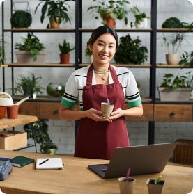 de eigenaresse van een plantenwinkel, glimlacht terwijl ze een kleine potplant vasthoudt.